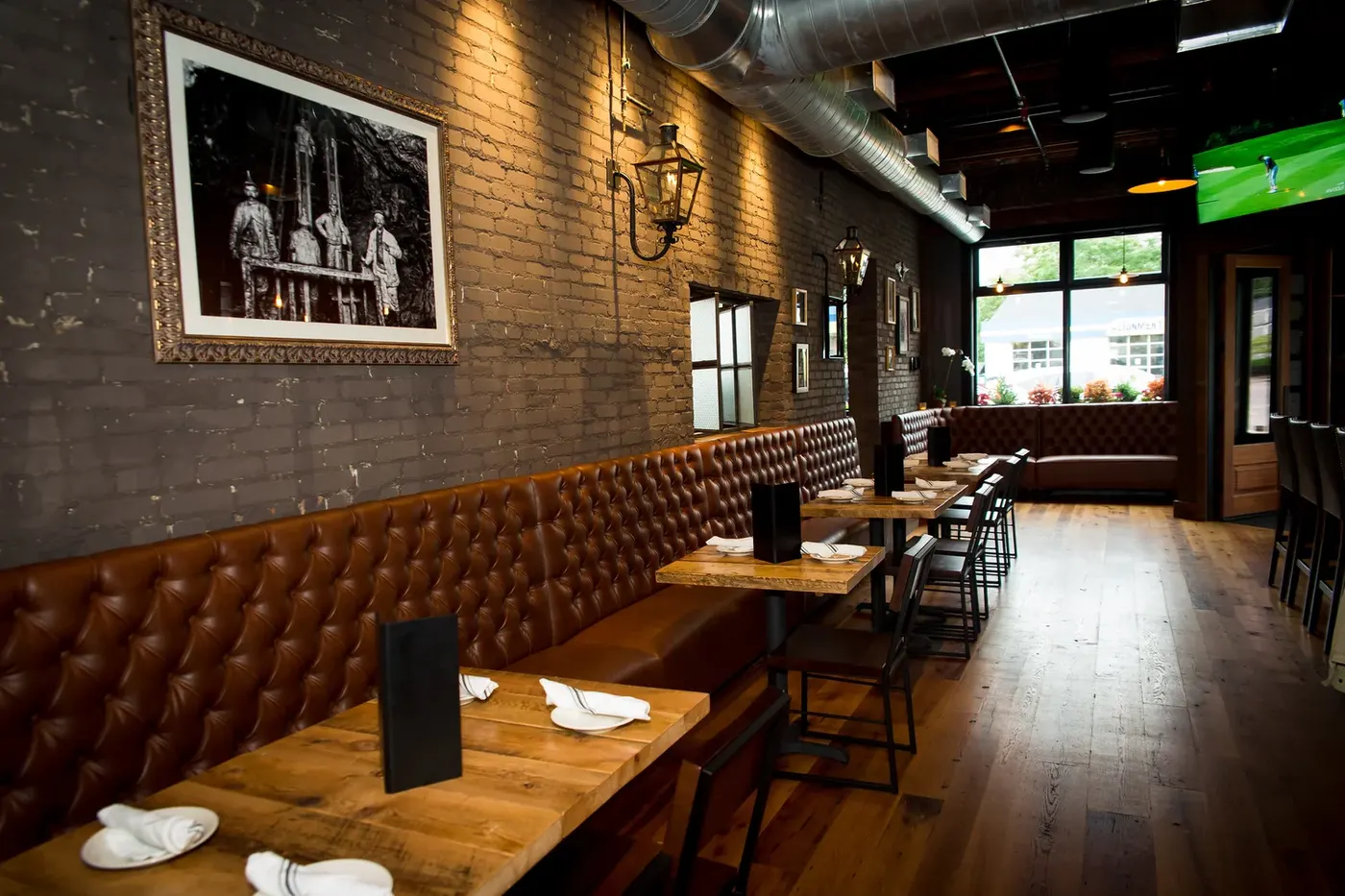 Leather banquette and wood tables along the brick wall at Brick & Beam Tavern
